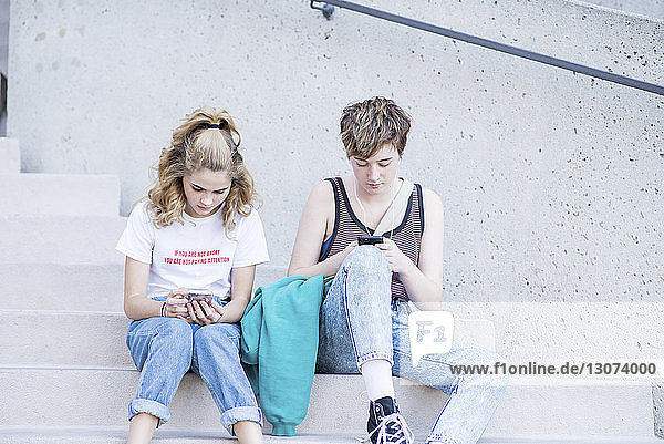 Freundinnen  die Smartphones benutzen  während sie auf Treppen in der Stadt sitzen