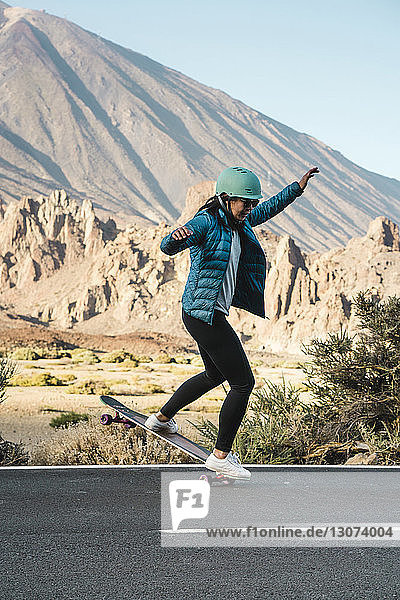 Full length of woman performing stunt on skateboard against mountain