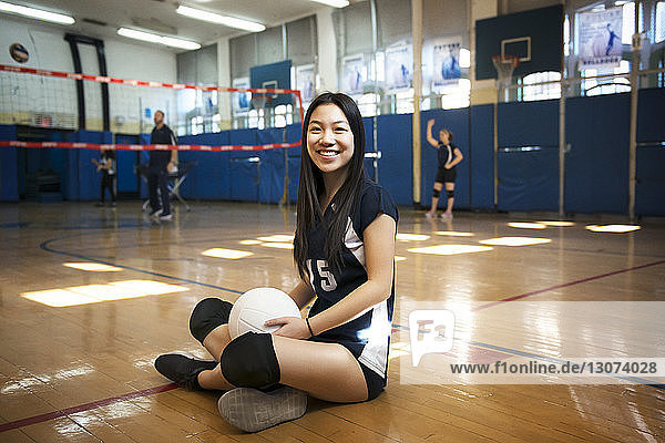Portrait of smiling girl holding ball and sitting on floor in volleyball court