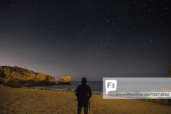 Rückansicht des am Strand stehenden Silhouettenmannes gegen das nächtliche Sternenfeld