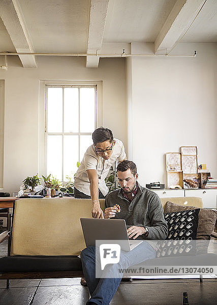 Businessman and colleague looking at laptop computer in creative office