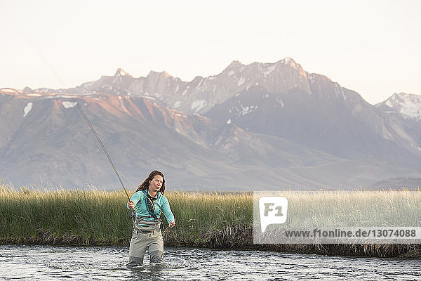 Young woman fly-fishing in Owens River against mountains