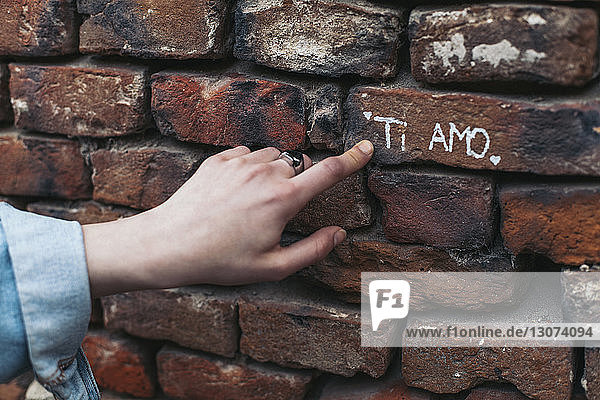 Geschnittene Hand einer Frau zeigt Text auf Ziegelsteinwand