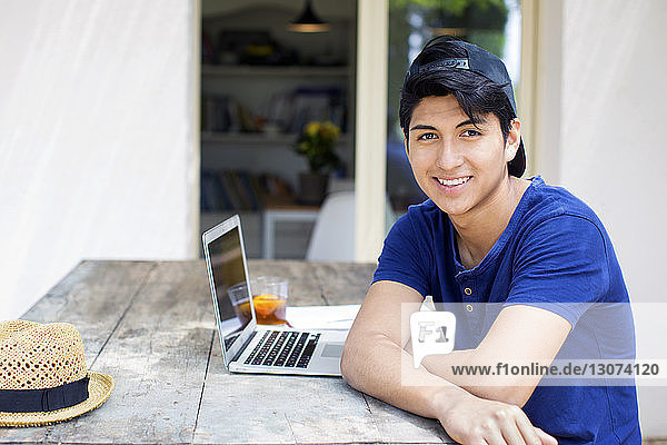 Portrait of happy man sitting with laptop at table in yard