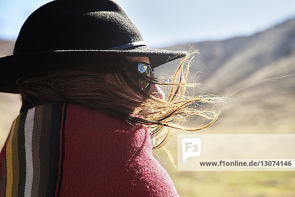 Rear view of woman with windswept hair wrapped in blanket at countryside