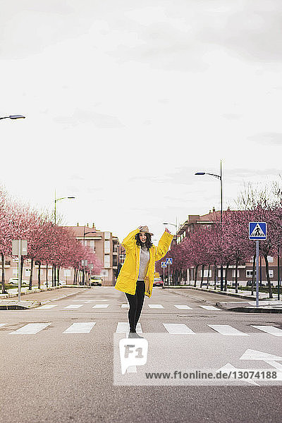 Junge Frau in gelbem Regenmantel in voller Länge im Skateboard auf der Straße gegen den Himmel in der Stadt