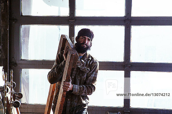 Portrait of worker carrying wooden equipment in workshop