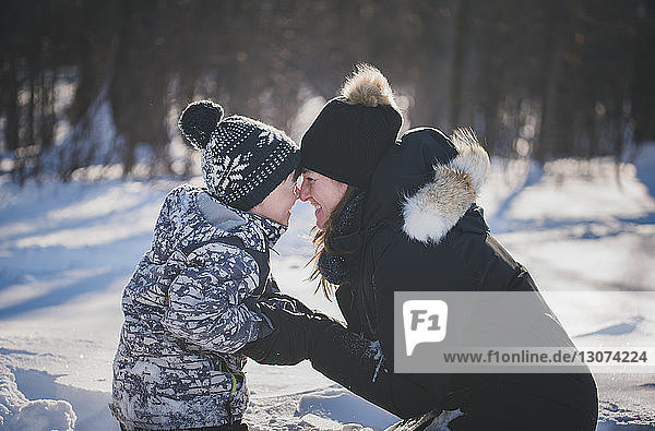 Verspielte Mutter und Sohn reiben sich auf verschneiter Wiese die Nasen