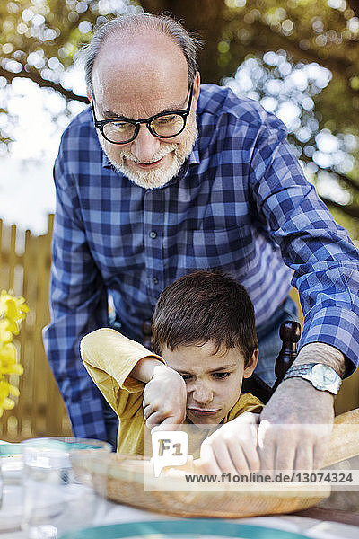 Lächelnder älterer Mann hilft Enkel beim Schneiden von Brotlaib