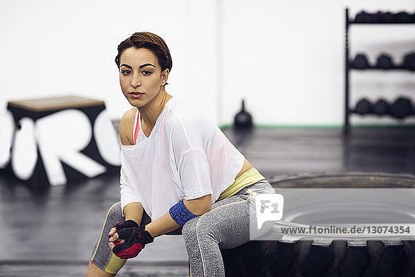 Porträt einer selbstbewussten Sportlerin  die im Fitnessstudio auf einem Reifen sitzt