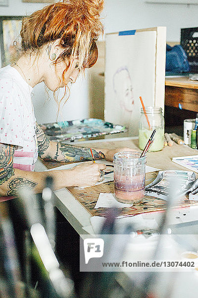 Seitenansicht einer Künstlerin  die im Atelier am Tisch stehend malt