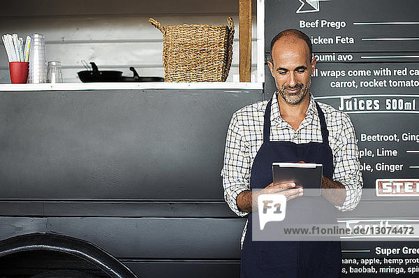 Smiling male owner using tablet computer while standing against food truck