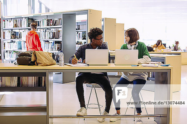 Freunde diskutieren während des Studiums über Laptop-Computer in der Bibliothek