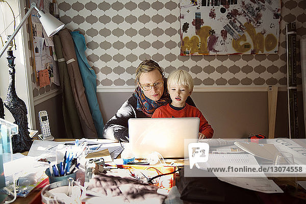 Mutter mit Sohn benutzt Laptop auf unordentlichem Tisch zu Hause