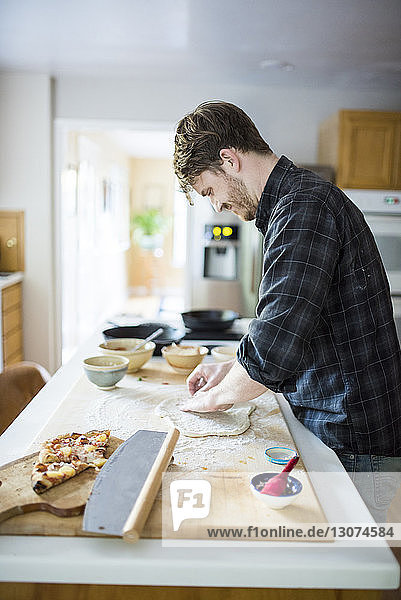 Seitenansicht eines Mannes  der zu Hause auf einer Kücheninsel Pizzateig knetet