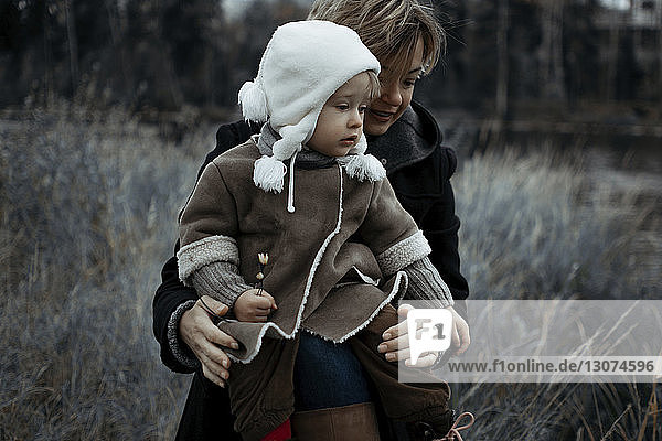 Mother with daughter sitting on grassy field at forest during winter