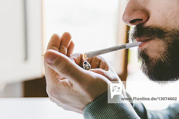 Bärtiger Mann zündet zu Hause mit Zigarettenanzünder einen Marihuana-Joint an