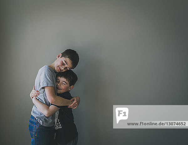 Lächelnde Brüder umarmen sich  während sie zu Hause an der Wand stehen