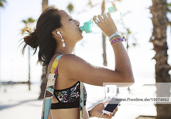 Seitenansicht einer sportlichen Frau  die am Strand Wasser trinkt