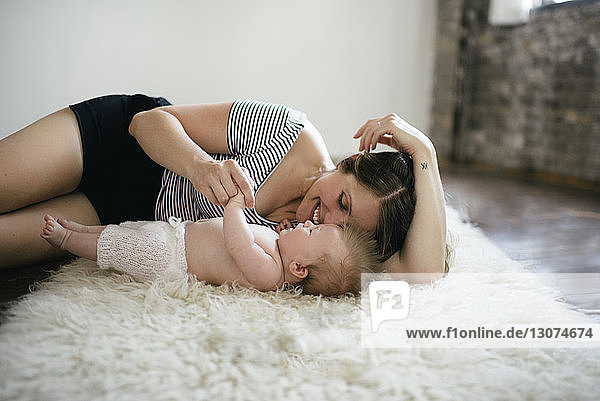 Mutter spielt mit Tochter  während sie zu Hause auf einem pelzigen Teppich liegt