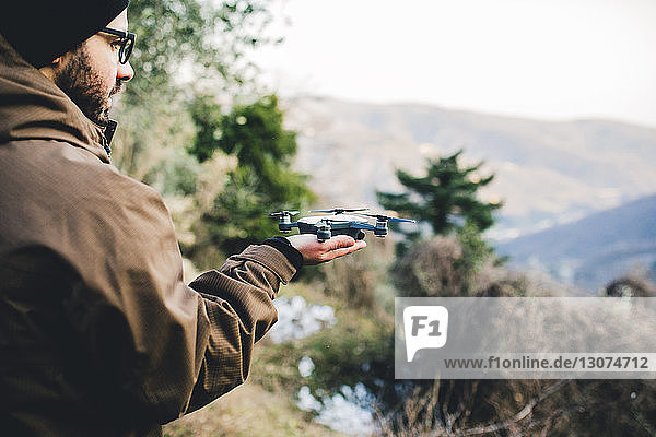 Side view of male hiker holding quadcopter while standing on mountain in forest