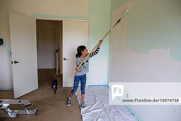 Girl painting wall using paint roller at home