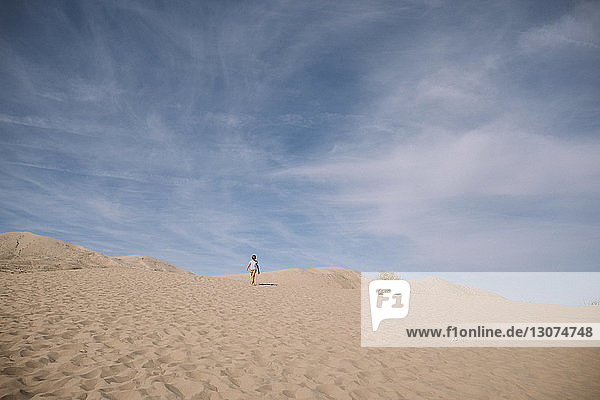 Mid distance view of boy against cloudy sky at desert during sunny day