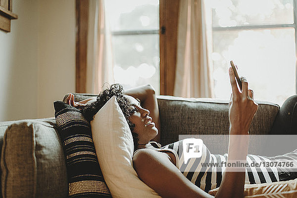 Seitenansicht einer Frau  die ein Smartphone benutzt  während sie zu Hause auf dem Sofa liegt