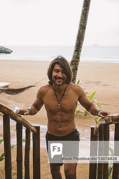 Porträt eines Mannes ohne Hemd  der am Strand an einem Holzgeländer steht