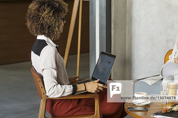 Side view of businesswoman with laptop sitting at hotel lobby