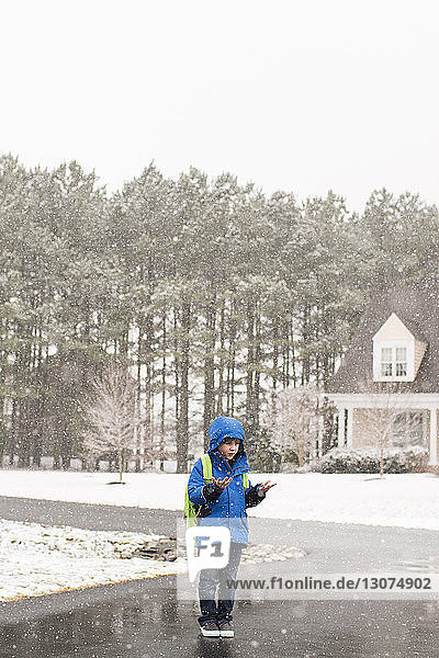 Junge geniesst Schnee  während er auf der Strasse gegen den klaren Himmel steht