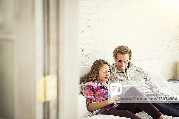 Vater und Tochter benutzen Tablet-Computer  während sie zu Hause im Bett sitzen