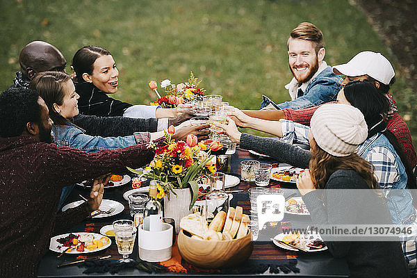 Happy friends toasting wine while sitting at table in backyard