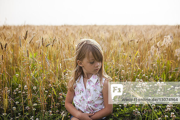 Upset girl sitting on field against sky in farm