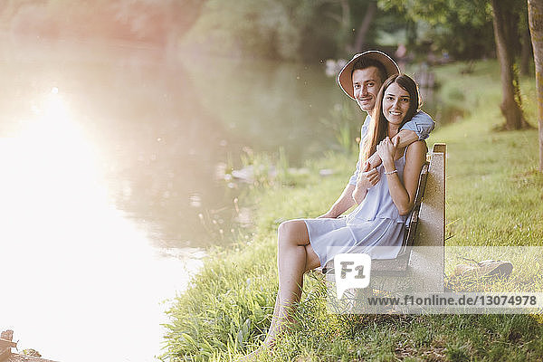 Portrait of couple sitting on bench by lake at park