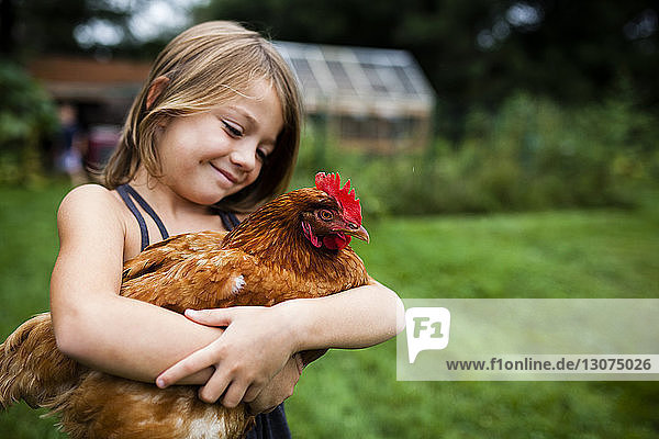 Lächelndes Mädchen hält Henne,  während es im Hof steht