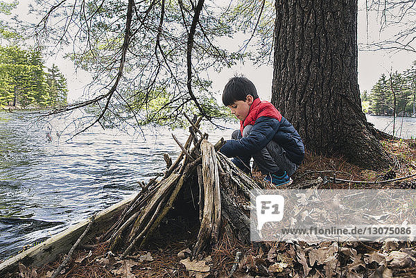 Full length of boy crouching by firewood on lakeshore in forest