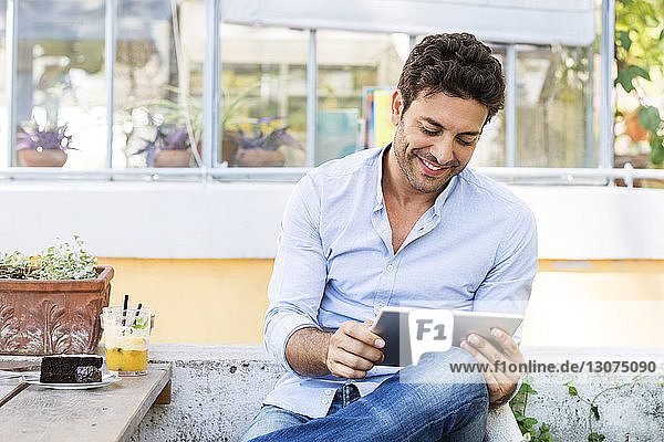 Smiling man using tablet computer while sitting at sidewalk cafe