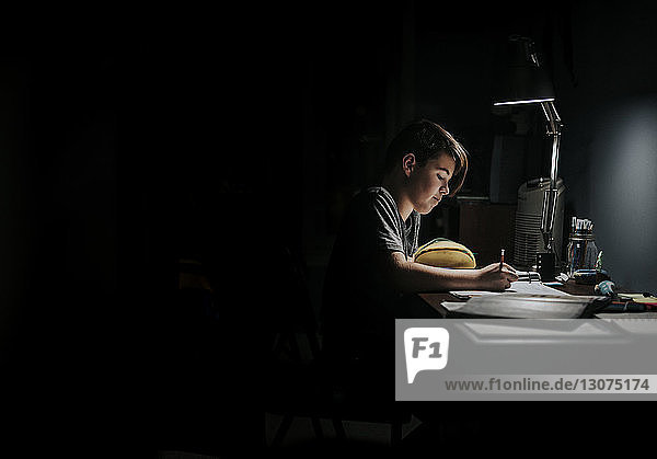 Seitenansicht eines Jungen  der am Tisch in der Dunkelkammer lernt