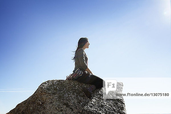 Seitenansicht einer Frau  die auf einem Felsen gegen den Himmel sitzt
