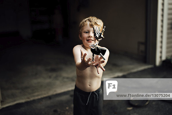 High angle view of shirtless boy throwing keys while standing against garage