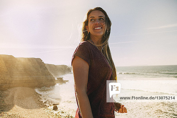 Lächelnde Frau schaut weg  während sie am Strand gegen den Himmel steht