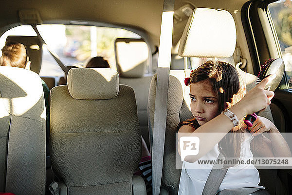 Mädchen kämmt Haare  während sie mit Geschwistern im Auto unterwegs ist