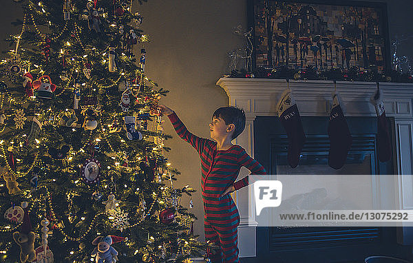 Junge mit Hand auf der Hüfte schaut auf beleuchteten Weihnachtsbaum