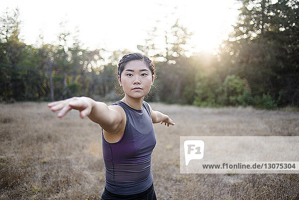 Porträt einer selbstbewussten Frau mit ausgestreckten Armen  die auf dem Feld Yoga praktiziert