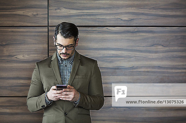 Businessman using smart phone while standing against wooden wall