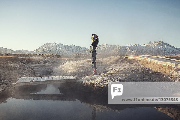 Side view of woman standing on rock at Mammoth Lake Hot Springs against clear sky