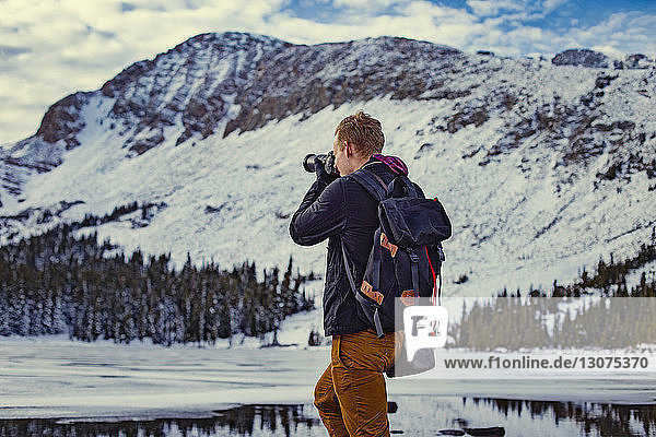 Rückansicht eines Mannes  der vor einem schneebedeckten Berg fotografiert