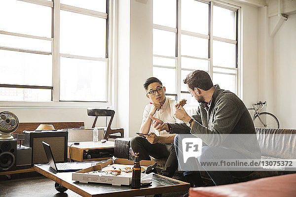 Geschäftsleute diskutieren beim Pizzaessen im Kreativbüro