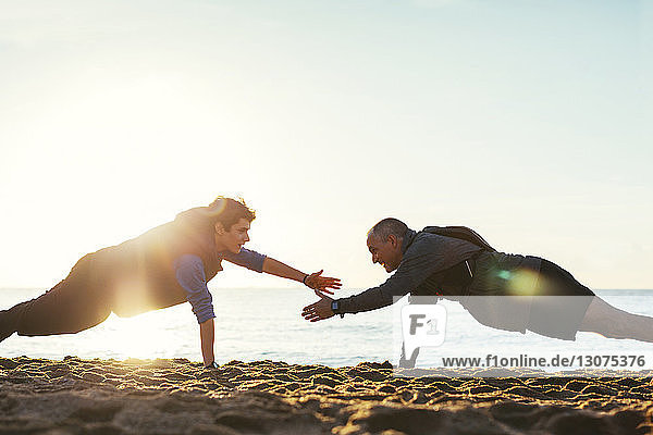 Side view of father and son doing push-ups together against clear sky at beach during sunset